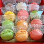 Assorted colorful macarons wrapped in clear bags arranged in a red gift box.
