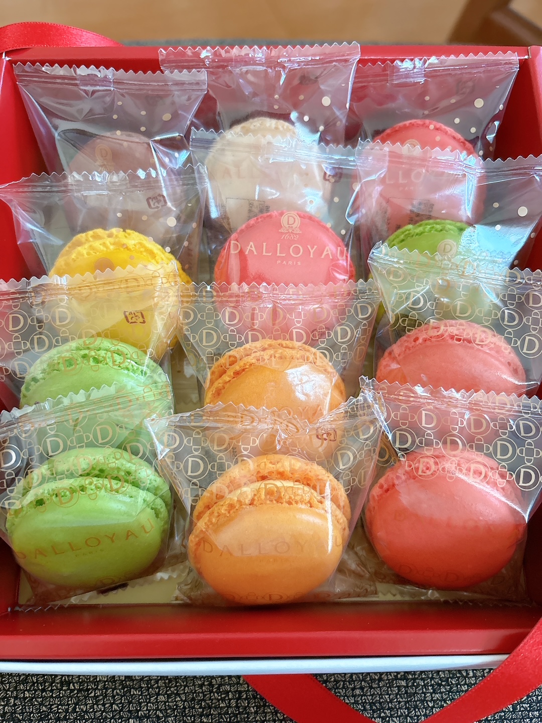 Assorted colorful macarons wrapped in clear bags arranged in a red gift box.