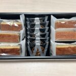 Assorted snack bars and cookies in a black gift box with clear wrappers and a central stack of dark snack bags.