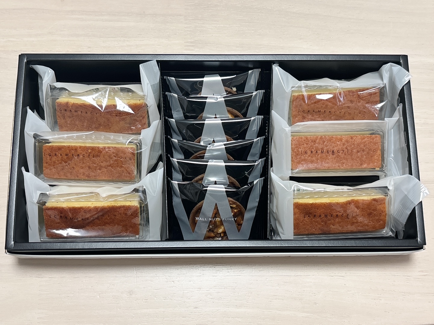 Assorted snack bars and cookies in a black gift box with clear wrappers and a central stack of dark snack bags.
