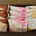 Assorted individually wrapped biscuits in a black box, with brown, pink, and yellow wrappers labeled ‘Biscuit au chocolat’ and ‘Sweet’/‘Strawberry’ flavors (Prince Hotels & Resorts).