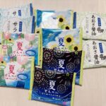 Assorted Japanese snack packages laid out on a light wooden surface, featuring summer-themed designs with sunflowers, fireworks, and colorful patterns.