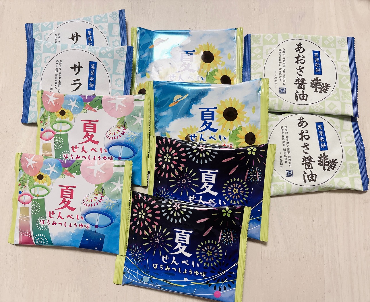 Assorted Japanese snack packages laid out on a light wooden surface, featuring summer-themed designs with sunflowers, fireworks, and colorful patterns.