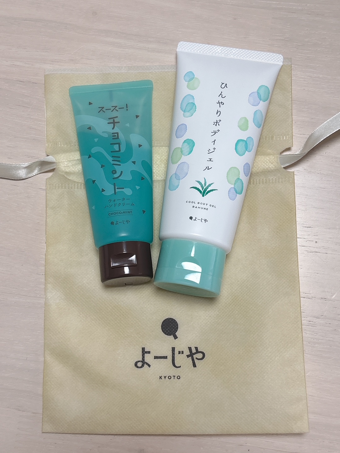 Two mint teal and white skincare tubes resting on a beige Yojiya bag with Kyoto logo visible.