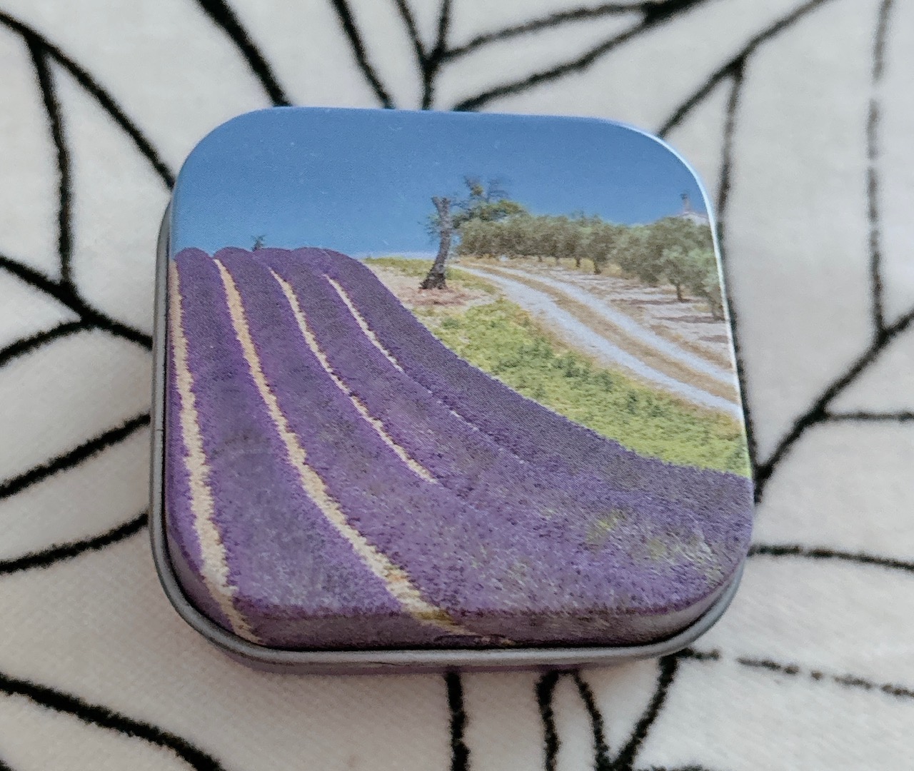 Compact metal tin featuring a lavender field illustration with purple rows and a dirt road under a blue sky