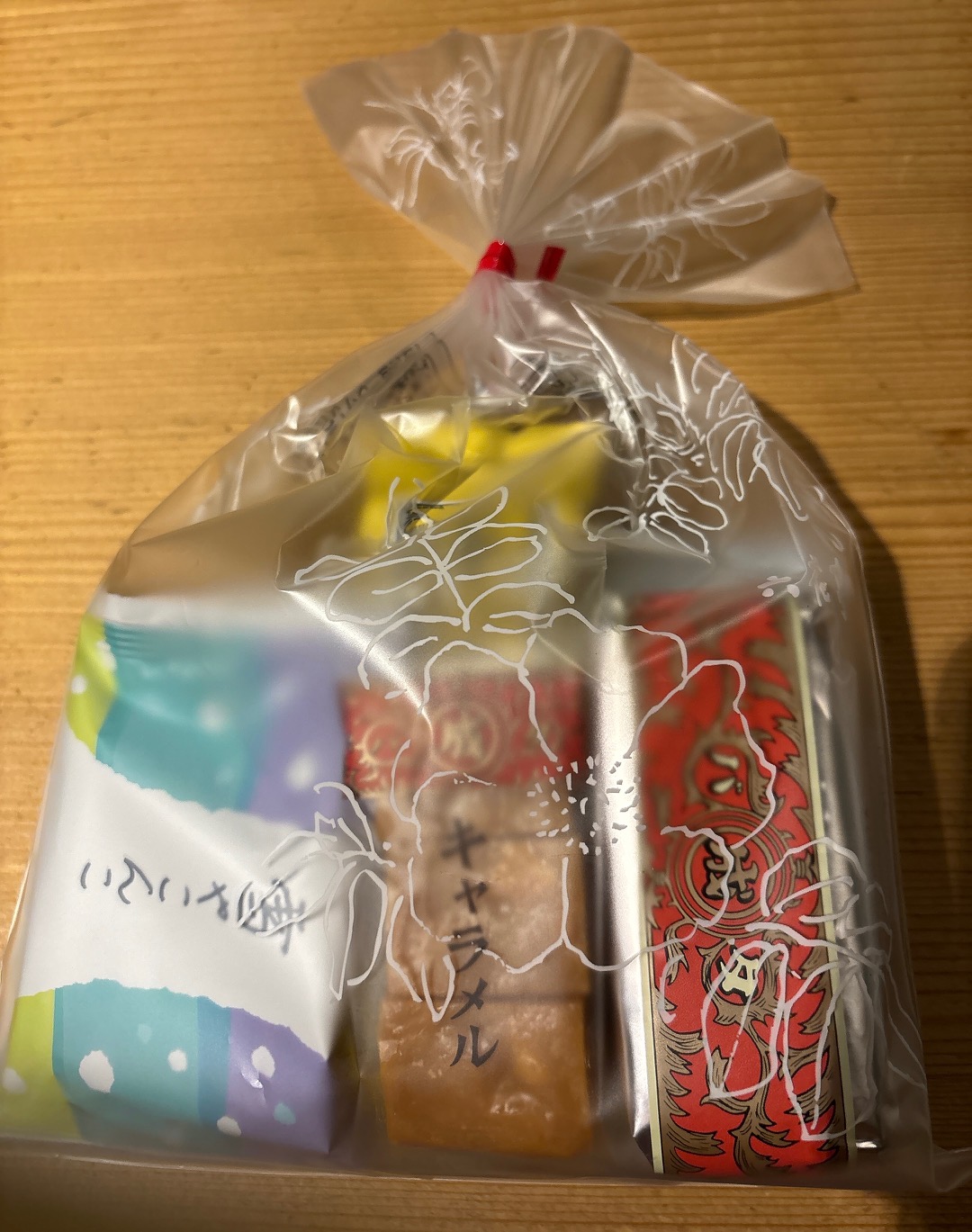 Clear plastic gift bag with a white floral pattern, tied with a red twist tie, revealing colorful snack boxes inside.