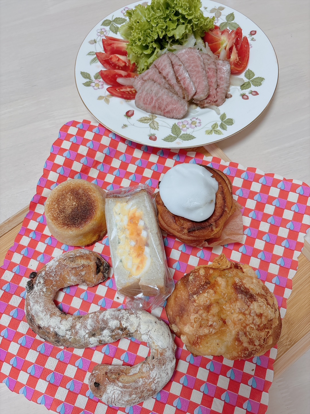 Plate with slices of roasted beef, lettuce, and tomato salad on a floral plate with greens beside it, on a light table.