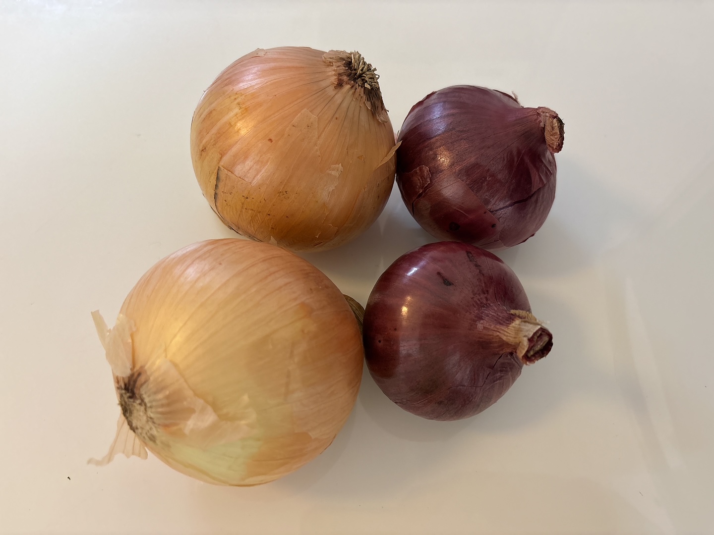 Four onions (two yellow, two red) arranged on a white surface for a cooking prep scene.