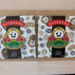 Two fabric gift packs on a brown surface, each with a colorful Daruma motif and a red Japanese banner on white patterned cloth.