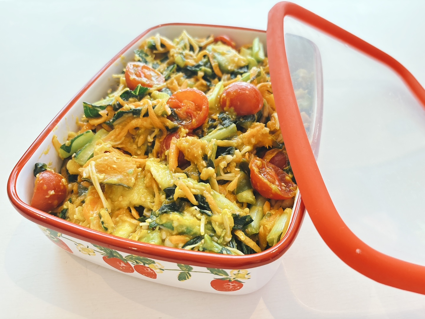 Enamel casserole dish with a colorful veggie pasta salad—tomatoes, greens, and shredded cheese in a yellow sauce, ready to serve.