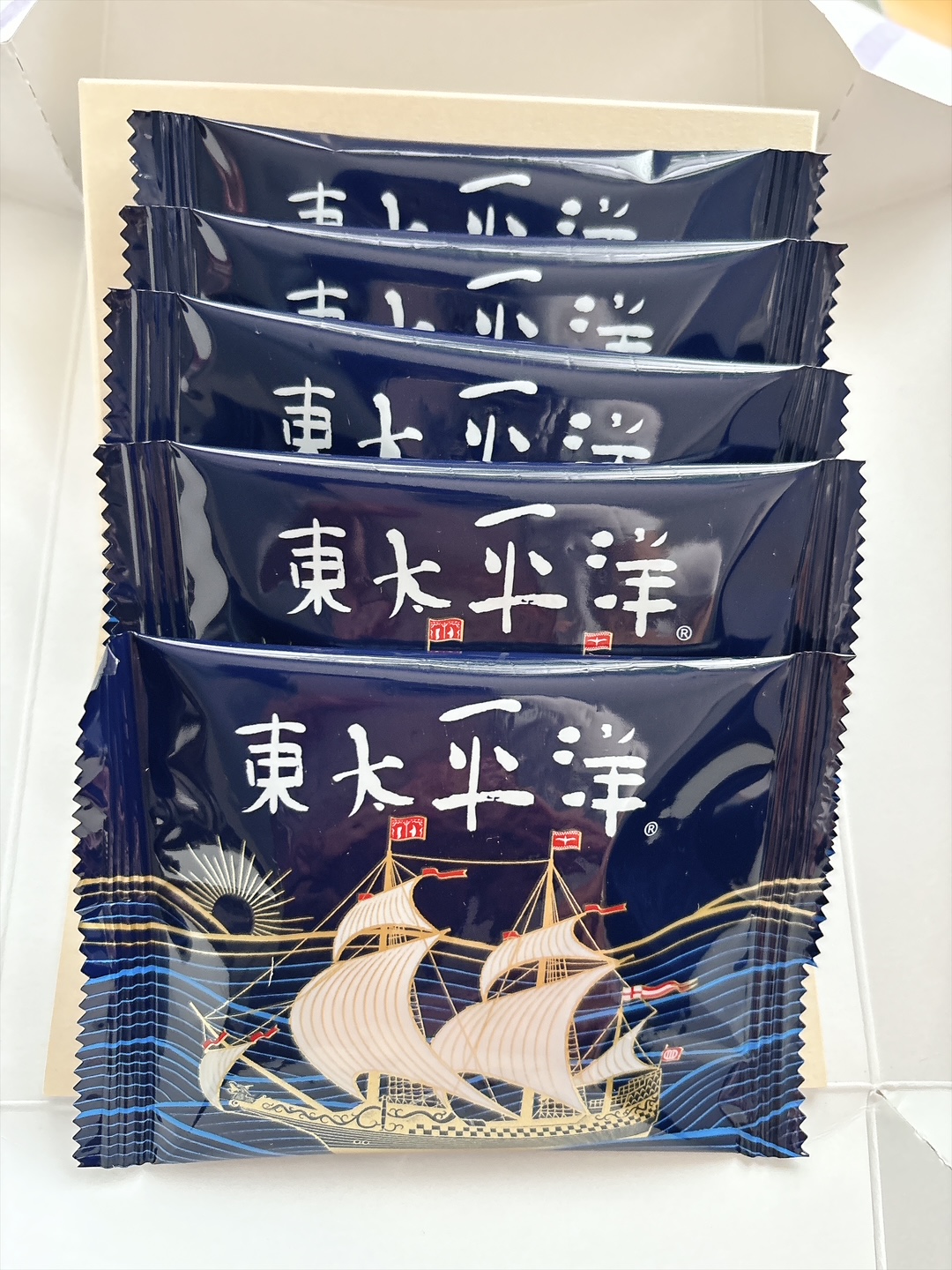 Five navy blue snack sachets stacked inside a box, each with white Chinese characters and a sailing-ship illustration on the bottom wrapper.