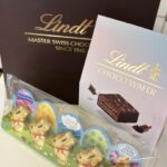 Lindt gift set with a dark box reading 'Lindt Master Swiss Chocolate Since 1845' and a lilac 'Choco Wafer' box, plus gold foil-wrapped eggs in a clear tray.