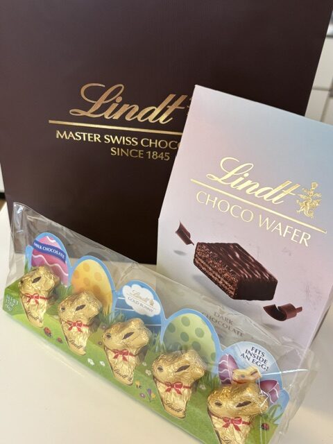 Lindt gift set with a dark box reading 'Lindt Master Swiss Chocolate Since 1845' and a lilac 'Choco Wafer' box, plus gold foil-wrapped eggs in a clear tray.