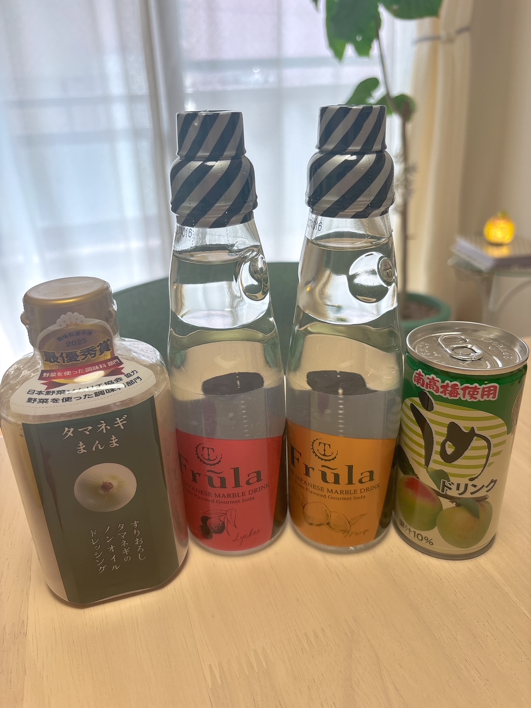 Assorted beverages on a light table: two glass bottles with striped caps, a green-labeled drink with Japanese text, and a peach-flavored can on the right.