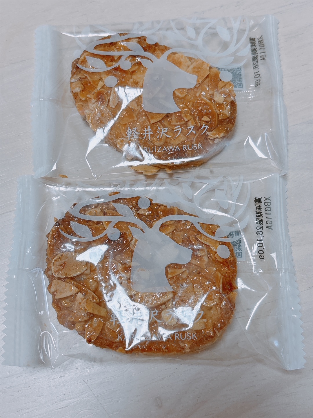Two almond-topped rusks sealed in clear bags with white decorative designs and the label 'KARUIZAWA RUSK' visible on each package.