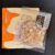 Bag of roasted peanuts in clear plastic package with Japanese text, placed on an orange and cream box/cover, likely a snack