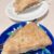 Triangular slice of baked pie with a golden, flaky crust and creamy fruit filling on a blue plate