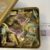 Gold tin open to reveal assorted individually wrapped hexagonal cookies or sweets in pink, yellow, and green wrappers with Japanese text on the wrappers.